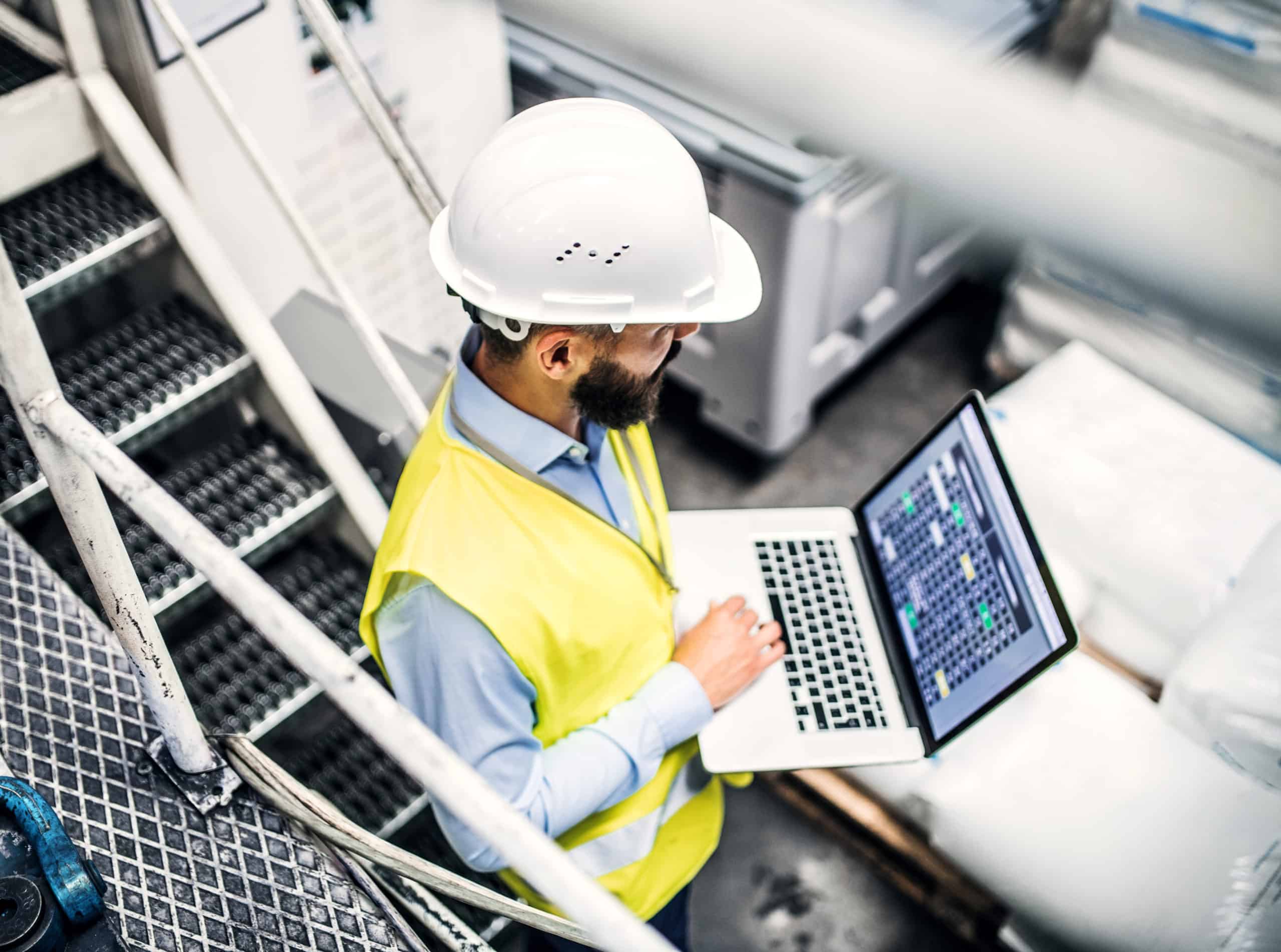 A portrait of an industrial man engineer with laptop in a factory, working.