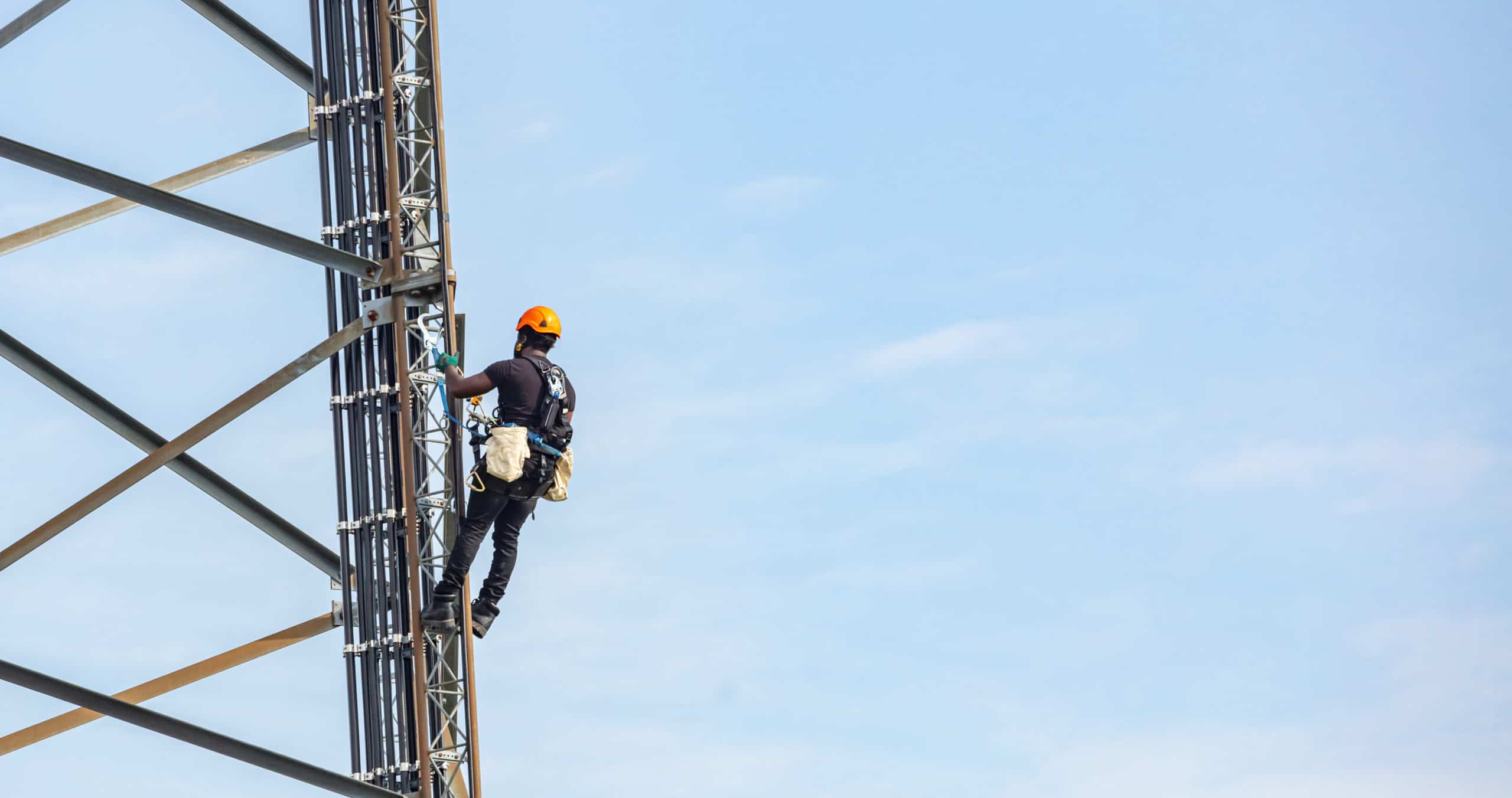 Telecom maintenance. Worker climber on tower against blue sky background